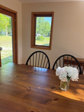 Een eettafel met stoelen, een raam met uitzicht op groen en een vaas met bloemen.