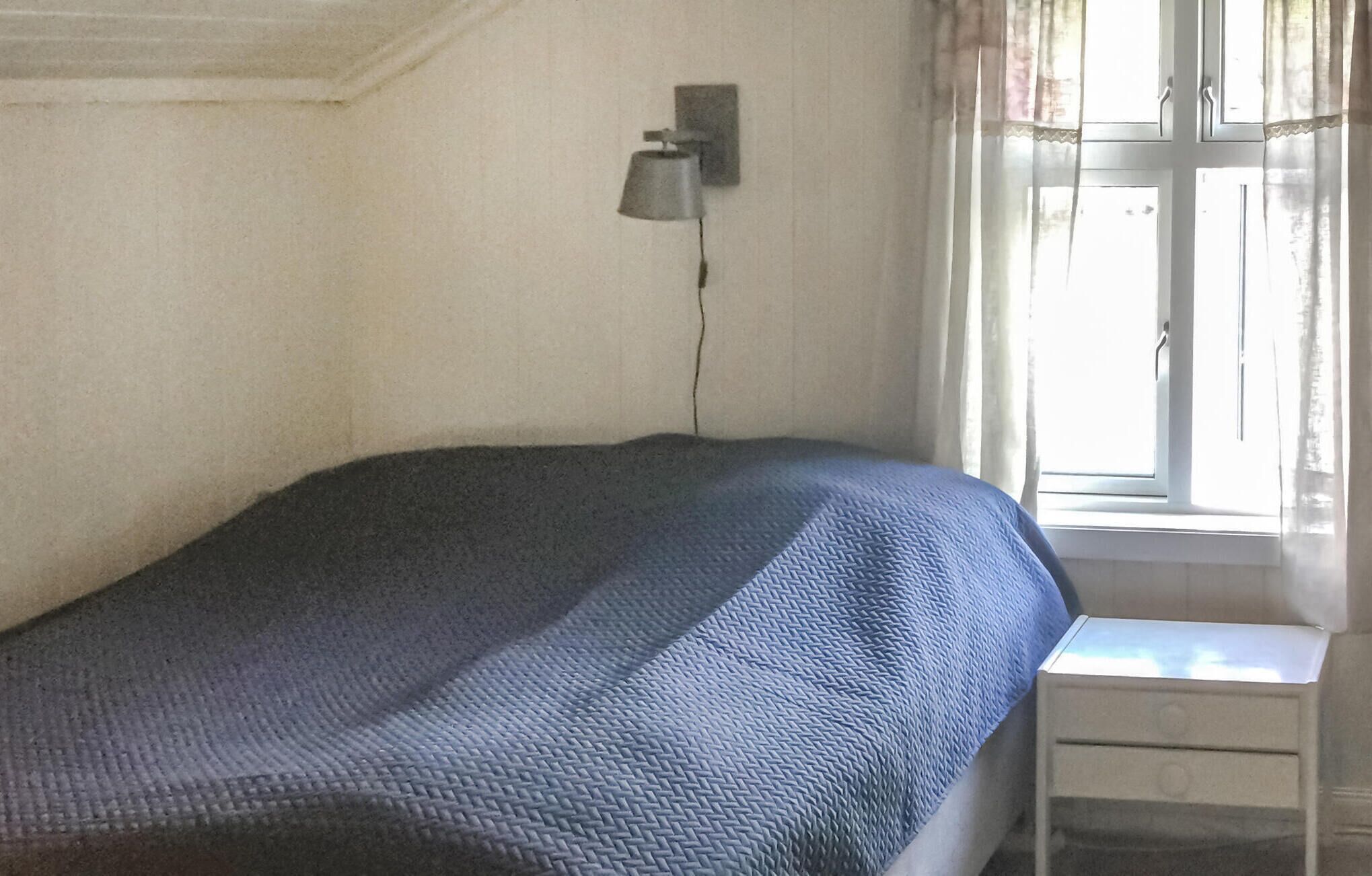 A single bed with a textured blanket, a bedside table with a lamp, and a window with curtains.