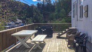 A wooden deck with a table and chairs, overlooking a dock with boats.