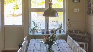 A dining table with chairs, a vase with flowers, and a window with plants and decorative items.