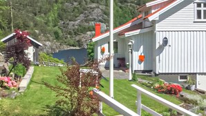 A white house with a red roof, a wooden deck, and a view of a lake surrounded by greenery.