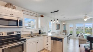 A modern kitchen with white cabinetry, stainless steel appliances, and a large island with a dishwasher. - "Sea Drift" Steps to the White Sand Beaches! Close to Restaurants, Coffee Shops! (Navarre)
