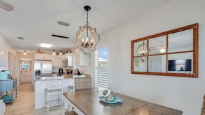 A modern kitchen with white cabinetry, a wooden dining table, and a chandelier. - "Sea Drift" Steps to the White Sand Beaches! Close to Restaurants, Coffee Shops! (Navarre)