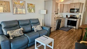 A compact living space with a sofa, a small table, a kitchenette, and wall art.