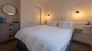 A bedroom with a bed, a dresser, a mirror, and wall-mounted lights.