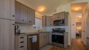 A modern kitchen with wooden cabinets, stainless steel appliances, and a window with blinds.