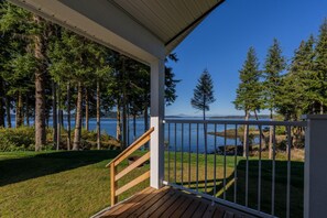 A wooden deck with a railing overlooking a lake, surrounded by tall trees.