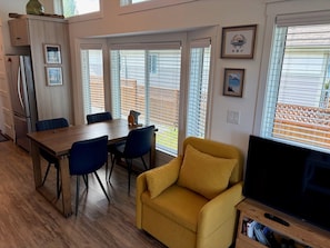 A modern kitchen with a dining area, a yellow armchair, and a television.