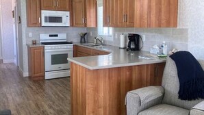 A compact kitchen with wooden cabinets, a microwave, an oven, and a small island. - 07 - Oceanside7 Cottage By The Sea at Alder Bay (Port McNeill)