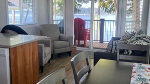 A cozy living room with a dining table, a sofa, and a chair. There is a ceiling fan and a view of the outdoors through large windows. - 07 - Oceanside7 Cottage By The Sea at Alder Bay (Port McNeill)