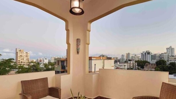 Ein Balkon mit Korbmöbeln, einem Glastisch und Blick auf die Stadt.