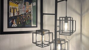 Ein gerahmtes Kunstwerk, das eine Straßenszene mit Menschen und Gebäuden zeigt, sowie eine moderne Leuchte mit mehreren quadratischen Rahmen und Leuchtmitteln.