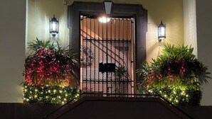 Ein verschlossener Eingangsbereich mit Zierpflanzen und Beleuchtung, ein Metallgittertor und zwei an der Wand befestigte Laternen.
