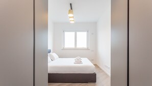 Ein modernes Schlafzimmer mit einem Bett, einem Fenster und einer Pendelleuchte.