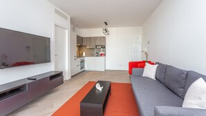 Ein modernes Wohnzimmer mit grauem Sofa, Flachbildfernseher und einem Holzessttisch.