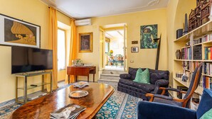 A living room with a flat-screen TV, a coffee table, a sofa, a bookshelf, and a patterned rug.