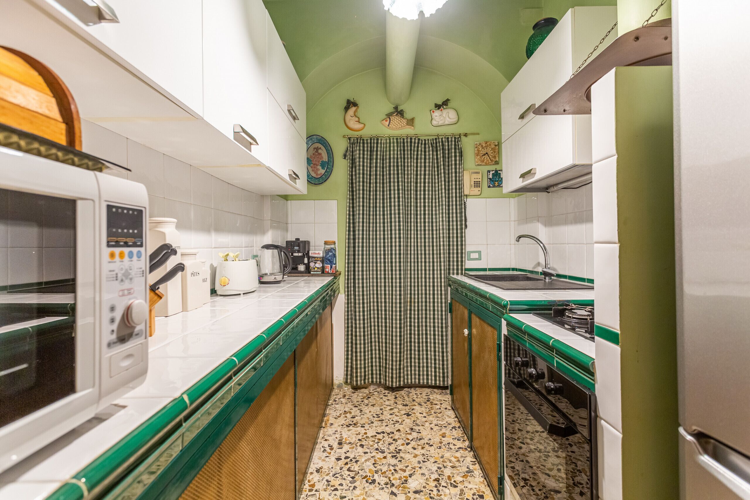 Una cocina con armarios blancos, microondas, cafetera y pileta.