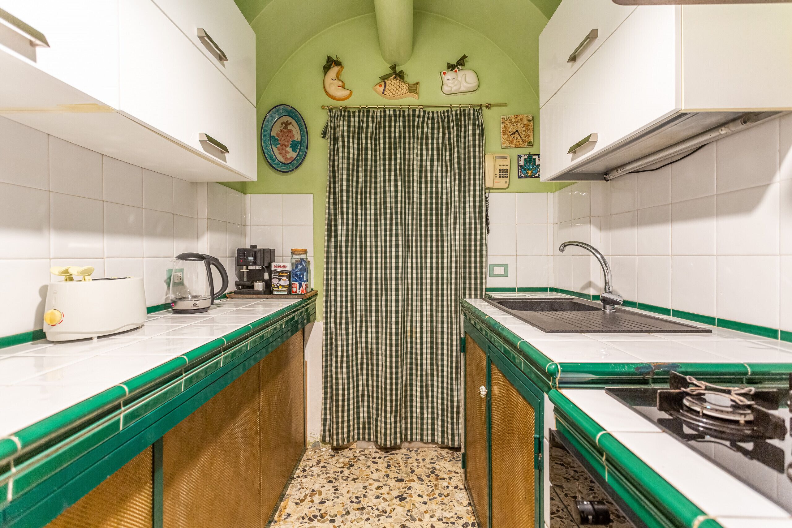 A kitchen with white cabinets, green countertops, a checkered curtain, and a tiled backsplash.