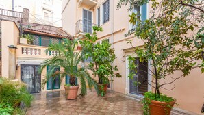 A courtyard with potted plants, a tiled floor, and a building with a balcony.