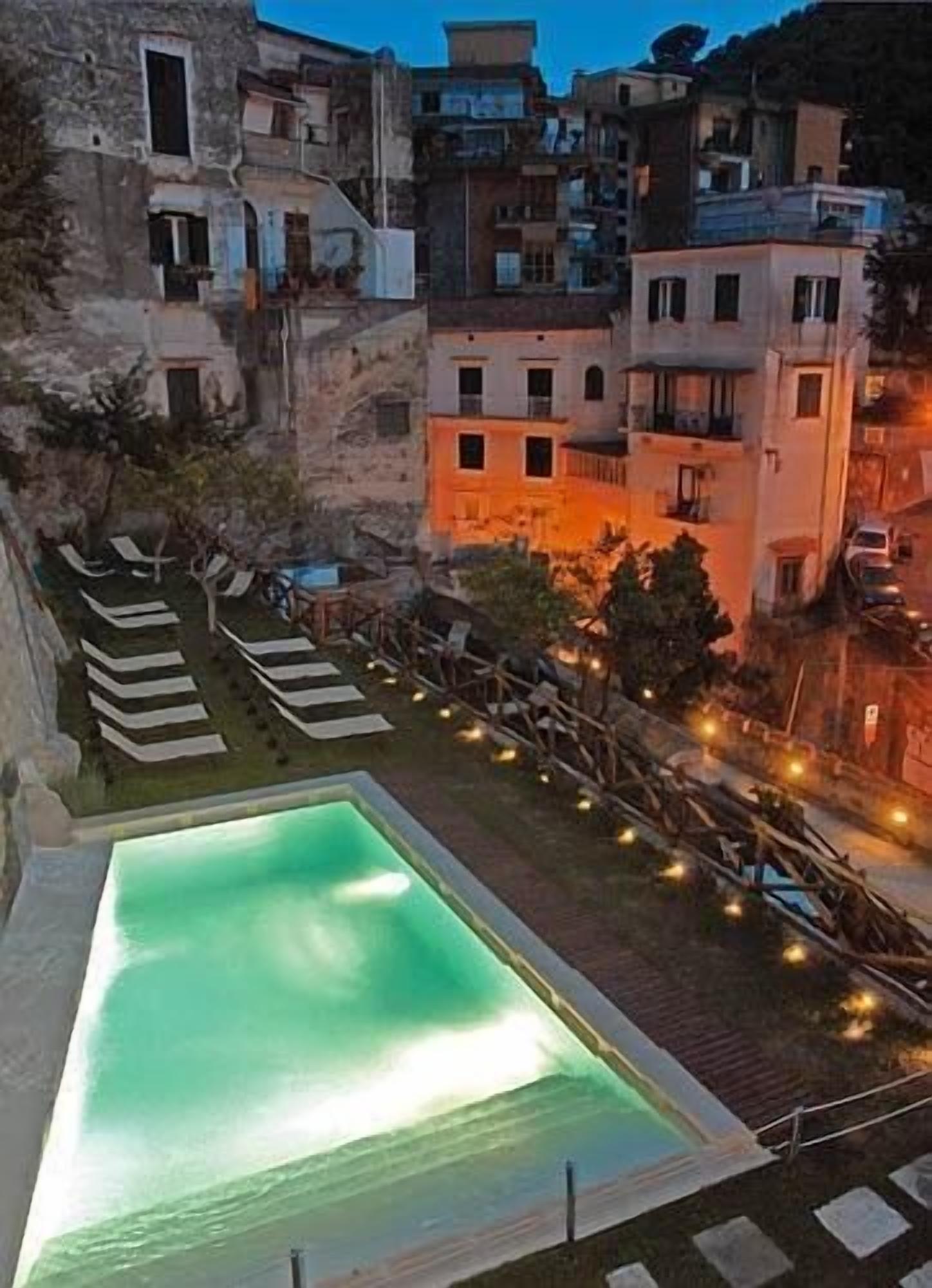 Ein Pool mit Liegestühlen, umgeben von Gebäuden und einem Nachthimmel.