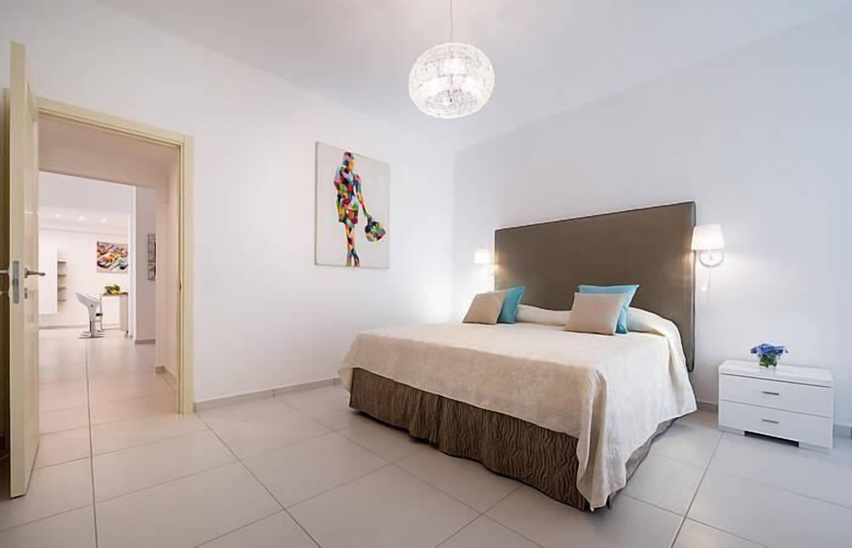 A modern bedroom with a large bed, a chandelier, and a painting on the wall.