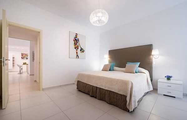 A modern bedroom with a large bed, a chandelier, and a painting on the wall.
