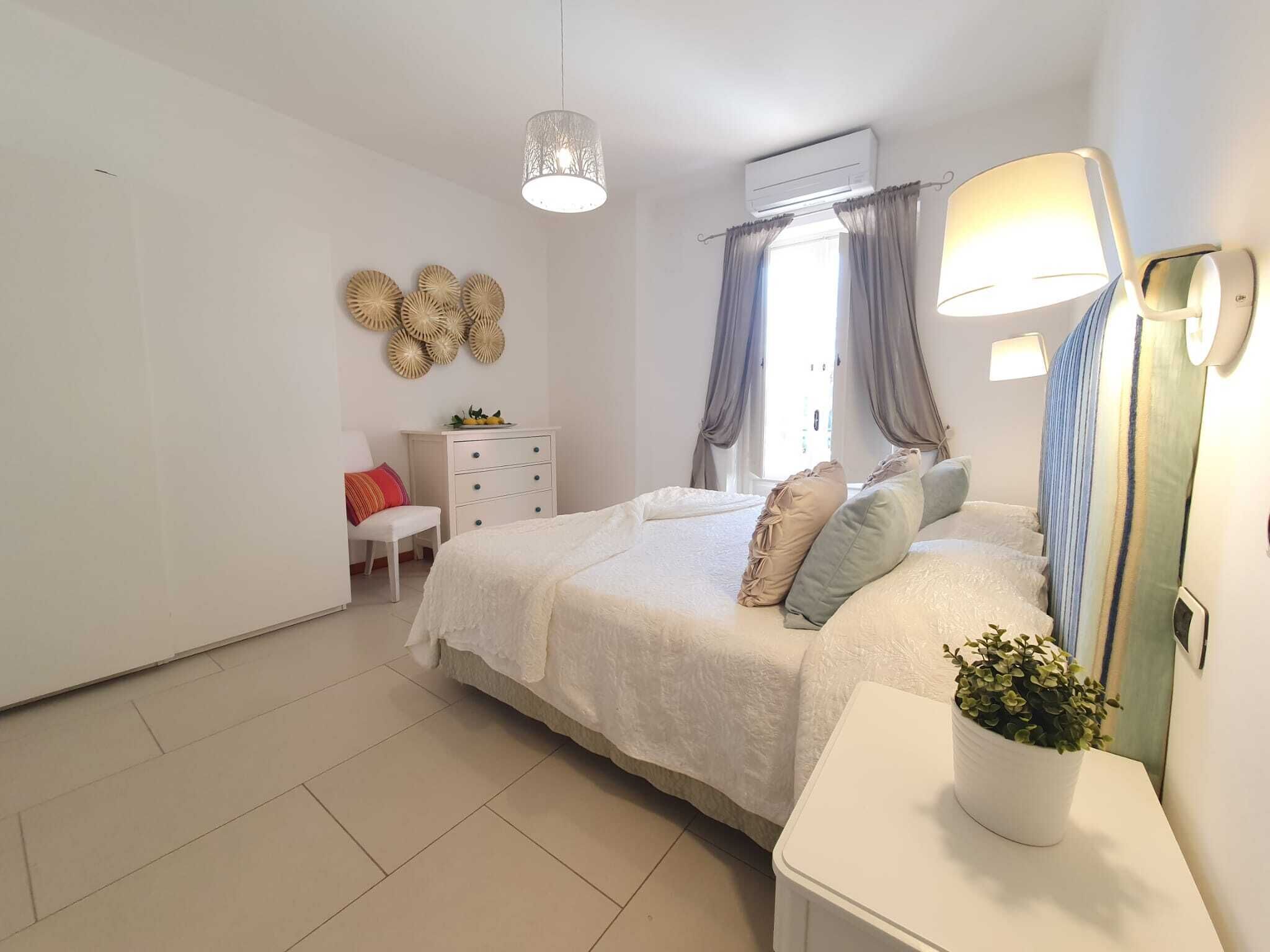 A bedroom with a bed, bedside table, lamp, air conditioning unit, and decorative wall art.