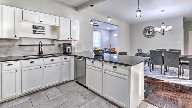 A modern kitchen with white cabinets, a black countertop, and a dining area with a table and chairs. - Peaceful Atascosa Home w/ Balcony & Deck! (Atascosa)