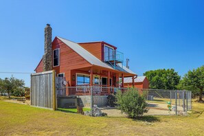 Ein rotes, zweistöckiges Haus mit einem Steinkamin, einem Balkon und einem umzäunten Garten.