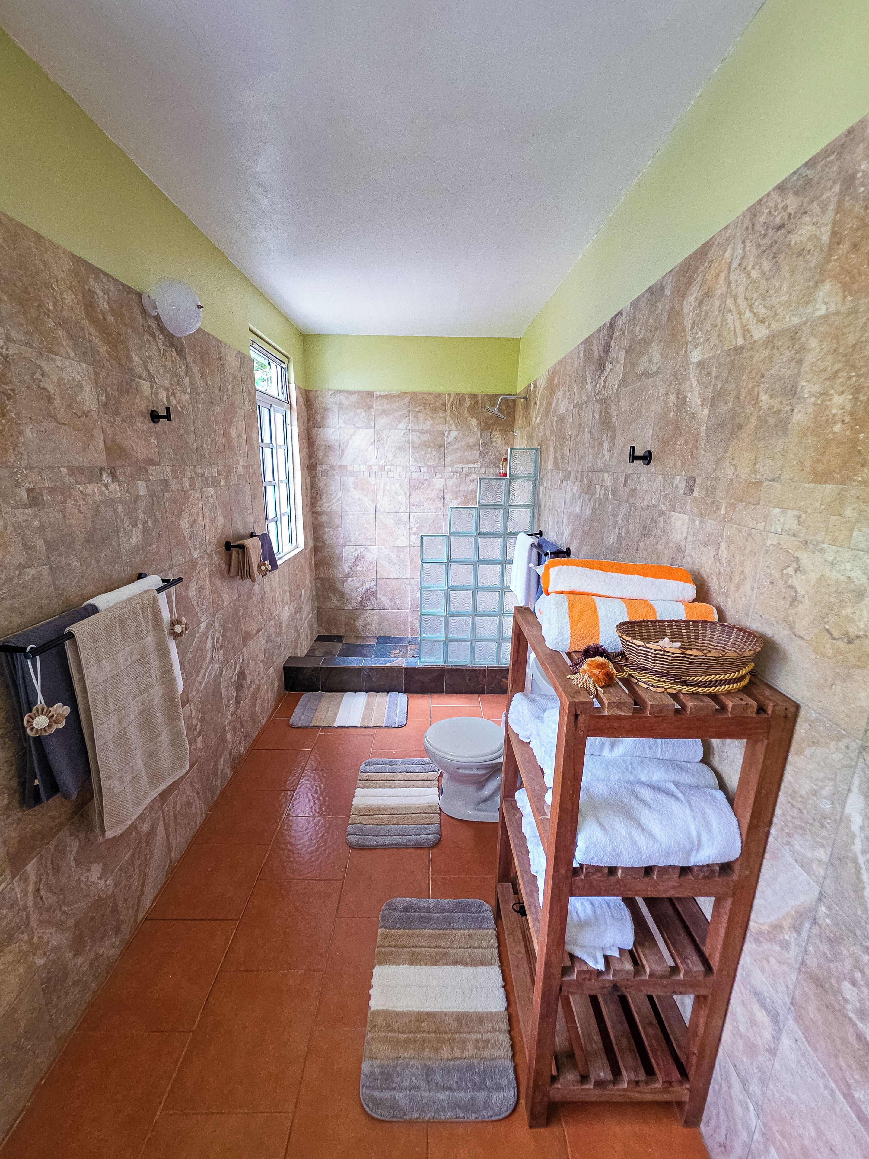 Un bagno con doccia, WC e una panca in legno con asciugamani.