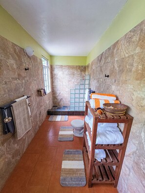 A bathroom with a shower, toilet, and a wooden bench with towels. - Oceanfront 3-bedroom villa with spectacular view! (Calibishie)