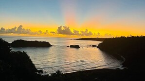 Un coucher de soleil sur la côte, avec une mer calme et des affleurements rocheux.