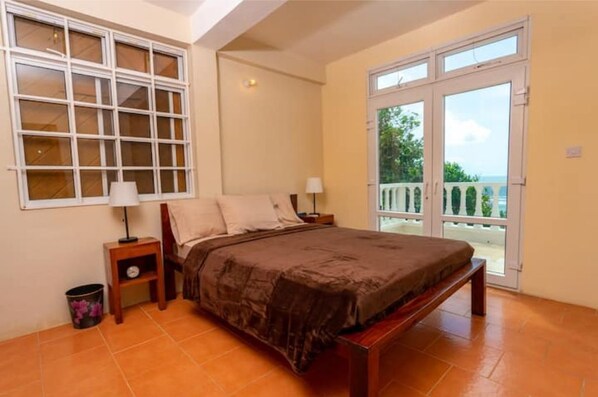 A bedroom with a large bed, a nightstand, a lamp, and a view of the outdoors through a sliding glass door. - Oceanfront 3-bedroom villa with spectacular view! (Calibishie)