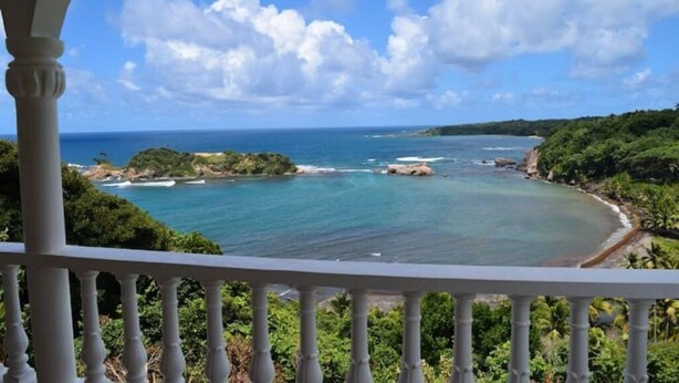Une vue sur la côte, prise depuis un balcon doté d’une balustrade, donnant sur une mer turquoise et un paysage verdoyant.