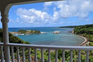 A coastal view from a balcony with a railing, overlooking a turquoise sea and a green landscape. - Oceanfront 3-bedroom villa with spectacular view! (Calibishie)