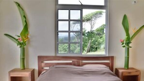 Une chambre à coucher avec une tête de lit en bois, une fenêtre donnant sur un paysage verdoyant et deux tables de chevet ornées de plantes.