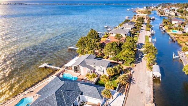 A coastal residential area with houses along a waterway, a bridge in the distance, and a swimming pool in the foreground.