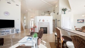 A spacious living room with a fireplace, a dining area with a long table, and a television in the corner.