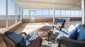 A covered outdoor seating area with wicker furniture and a view of the ocean.