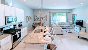 Una cocina moderna con una isla central, armarios blancos, electrodomésticos de acero inoxidable e iluminación colgante.
