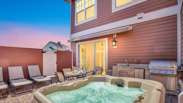 Un patio trasero con jacuzzi, mobiliario exterior y una parrilla.