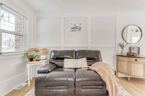 Et værelse med en brun lædersofa, et lille sofabord med en lampe, et spejl og et billede i ramme på væggen.