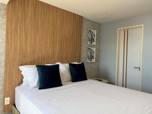 A bedroom with a wooden headboard, a bed with white and dark pillows, and two leaf-patterned wall art pieces.
