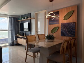 A modern dining area with a wooden table, chairs, a potted plant, and artwork on the walls. - Imperial Bessa (João Pessoa)