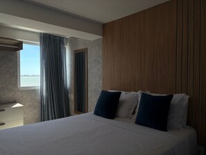 Habitación de hotel con una cama, una ventana con cortinas, una pared de madera y vista al agua.