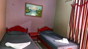 Una habitación con dos camas, una mesita de noche, un cuadro en la pared y una cortina.