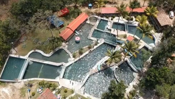 Vista aérea de un resort con varias piscinas, palmeras y un edificio de techo rojo.
