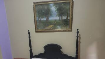 A bed with a white mattress and a blue towel, two wooden nightstands, and a framed painting of a forest scene on the wall.