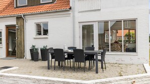 Une terrasse avec une table et des chaises, un mur en briques blanches et une fenêtre donnant sur la rue.