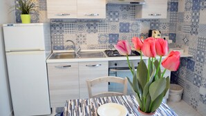 Une cuisine avec des carreaux décoratifs, un évier, des placards, une cuisinière et une table à manger avec une assiette et une plante en pot.